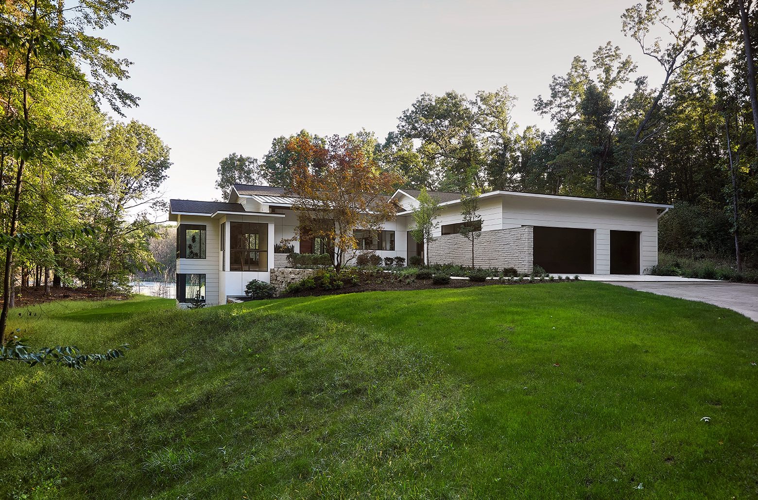 White modern home set into a small hill with trees around and a lake behind