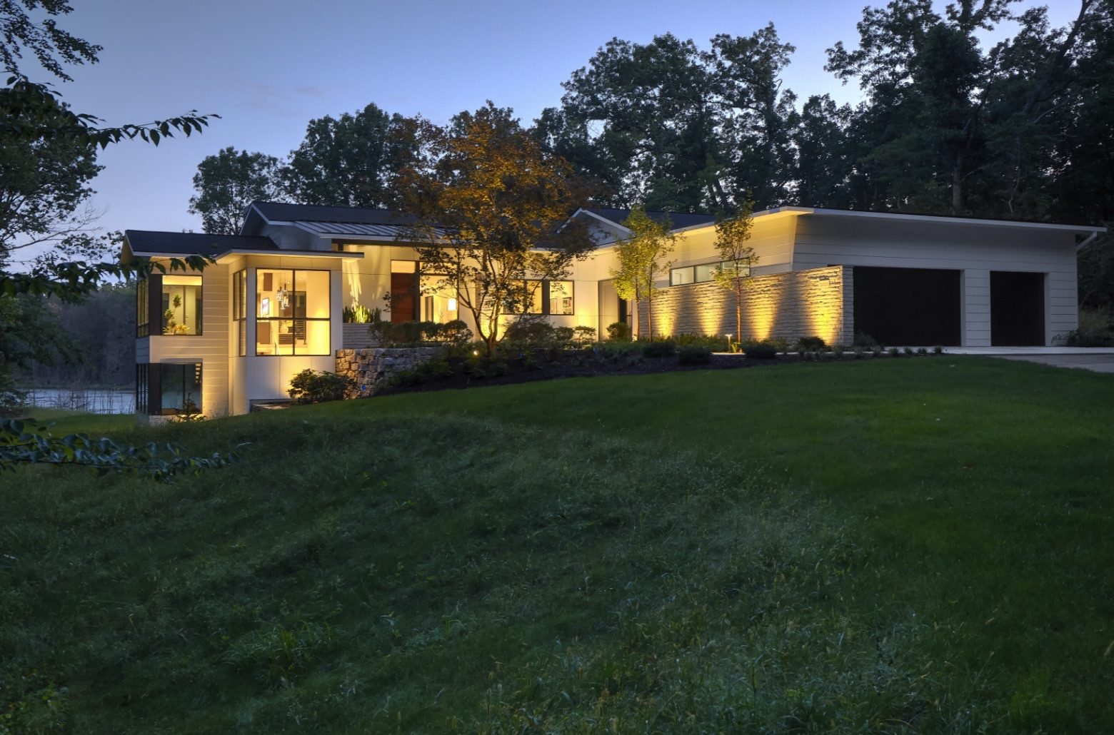 A white modern home set into a hill with beautiful illumination at night